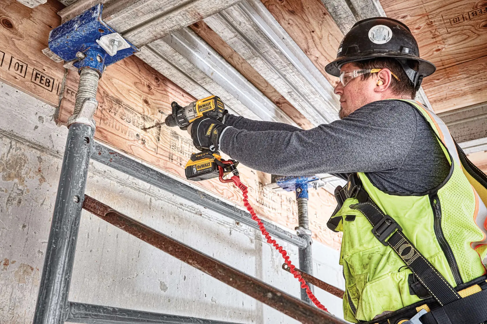Eine Person verwendet einen kabellosen DEWALT-Bohrer (Modell DCD996P2), um einen Holzbalken auf einer Baustelle zu bohren.