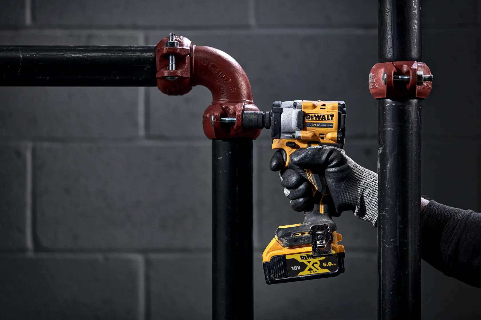 Eine Person mit schwarzen Handschuhen verwendet ein gelbes kabelloses DEWALT Elektrowerkzeug, um eine Metallrohrverbindung festzuziehen.