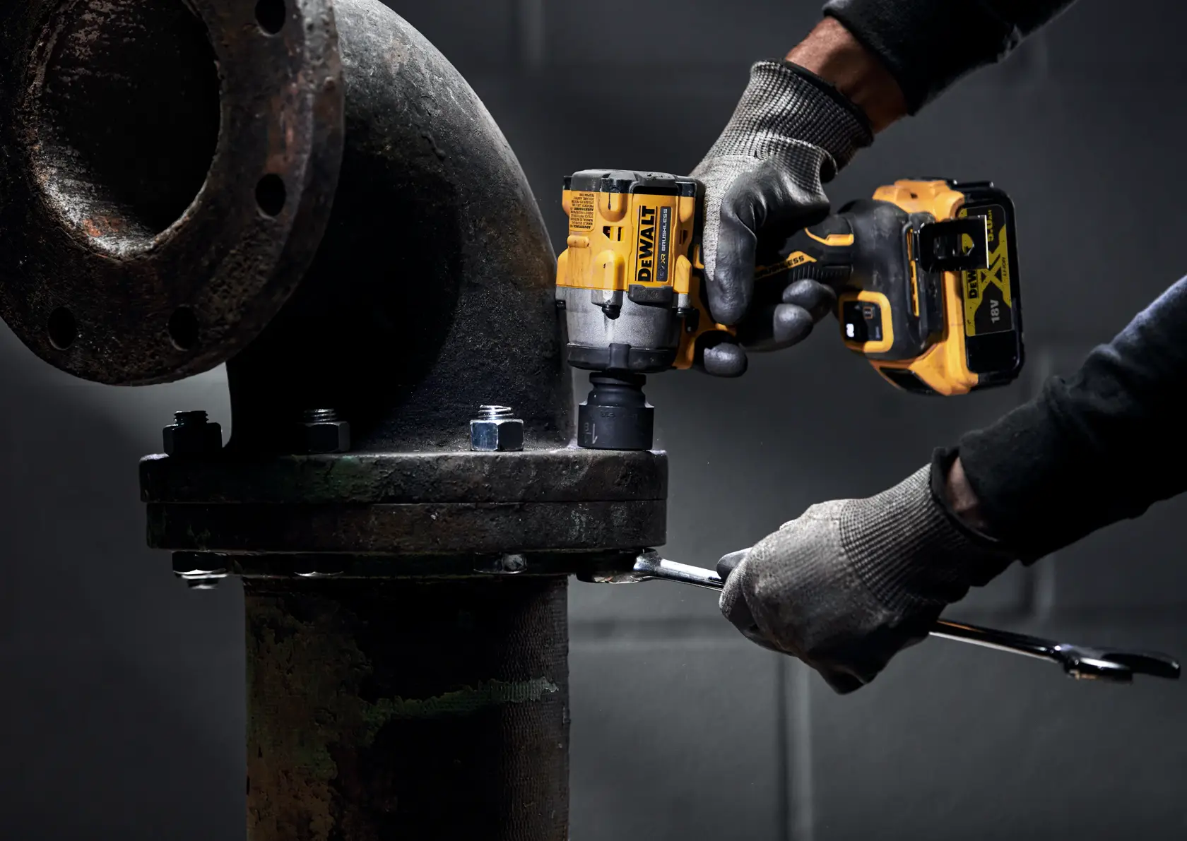 Una persona con guantes usa una llave de impacto inalámbrica DEWALT para apretar los pernos en una gran brida de tubería industrial.