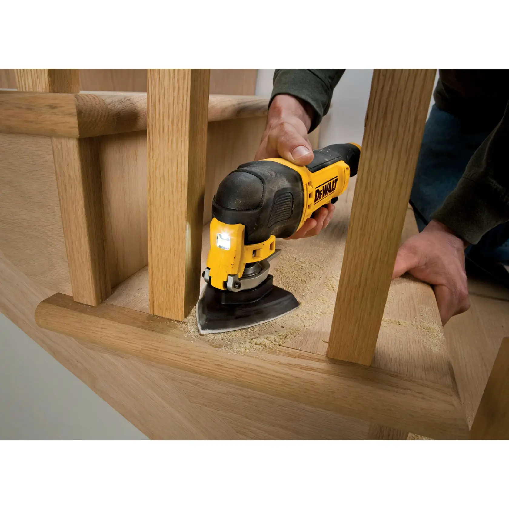 Herramienta oscilante DEWALT lijando madera cerca de una escalera, persona sostiene, aserrín visible.