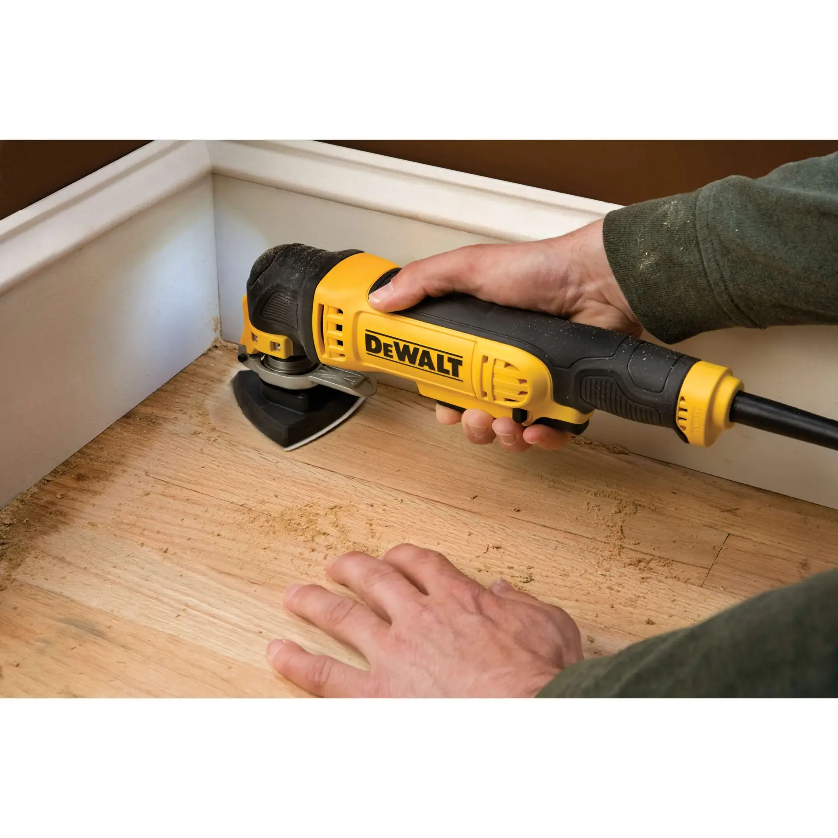 Herramienta DEWALT DT3095 lijando suelo de madera cerca del zócalo, sostenida a mano.