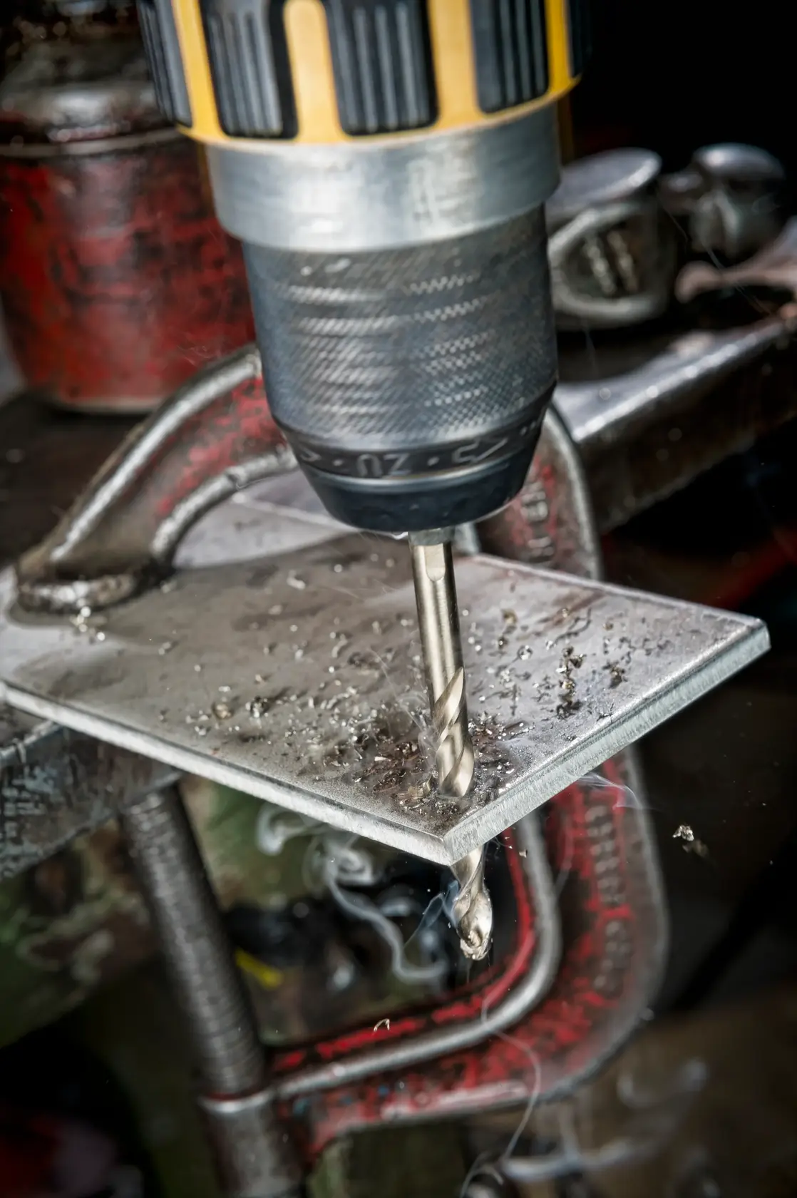 Close-up of a DEWALT drill making a hole in a metal sheet clamped to a workbench.