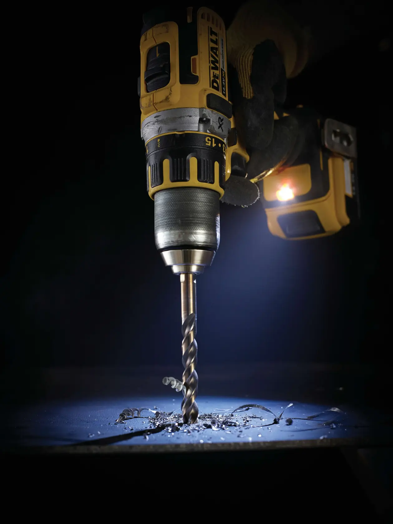 Taladro inalámbrico DEWALT con broca DT5557 perforando metal, virutas y área de trabajo iluminada.