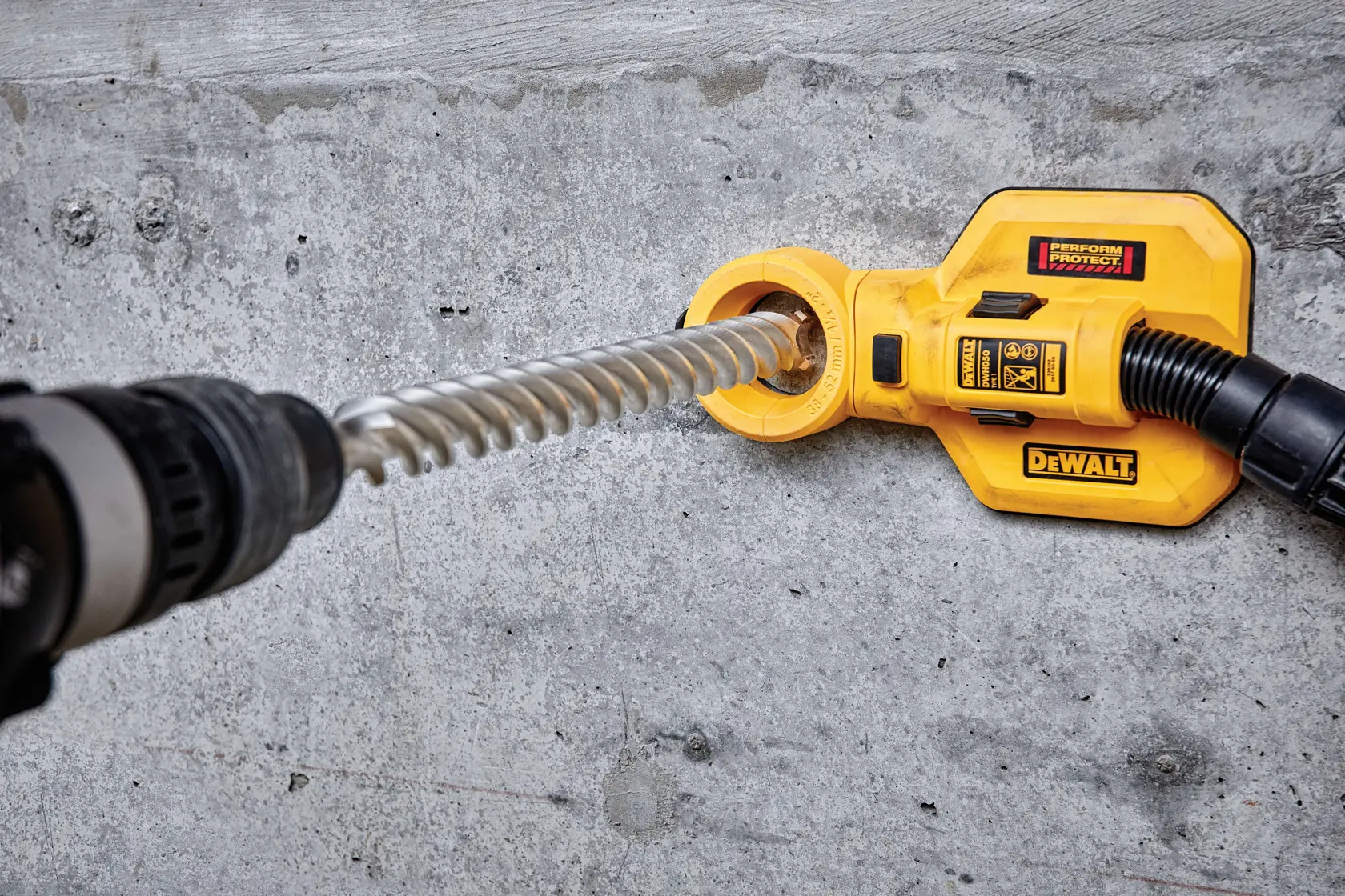 Accesorio DEWALT en pared de concreto con taladro y manguera para extracción de polvo.