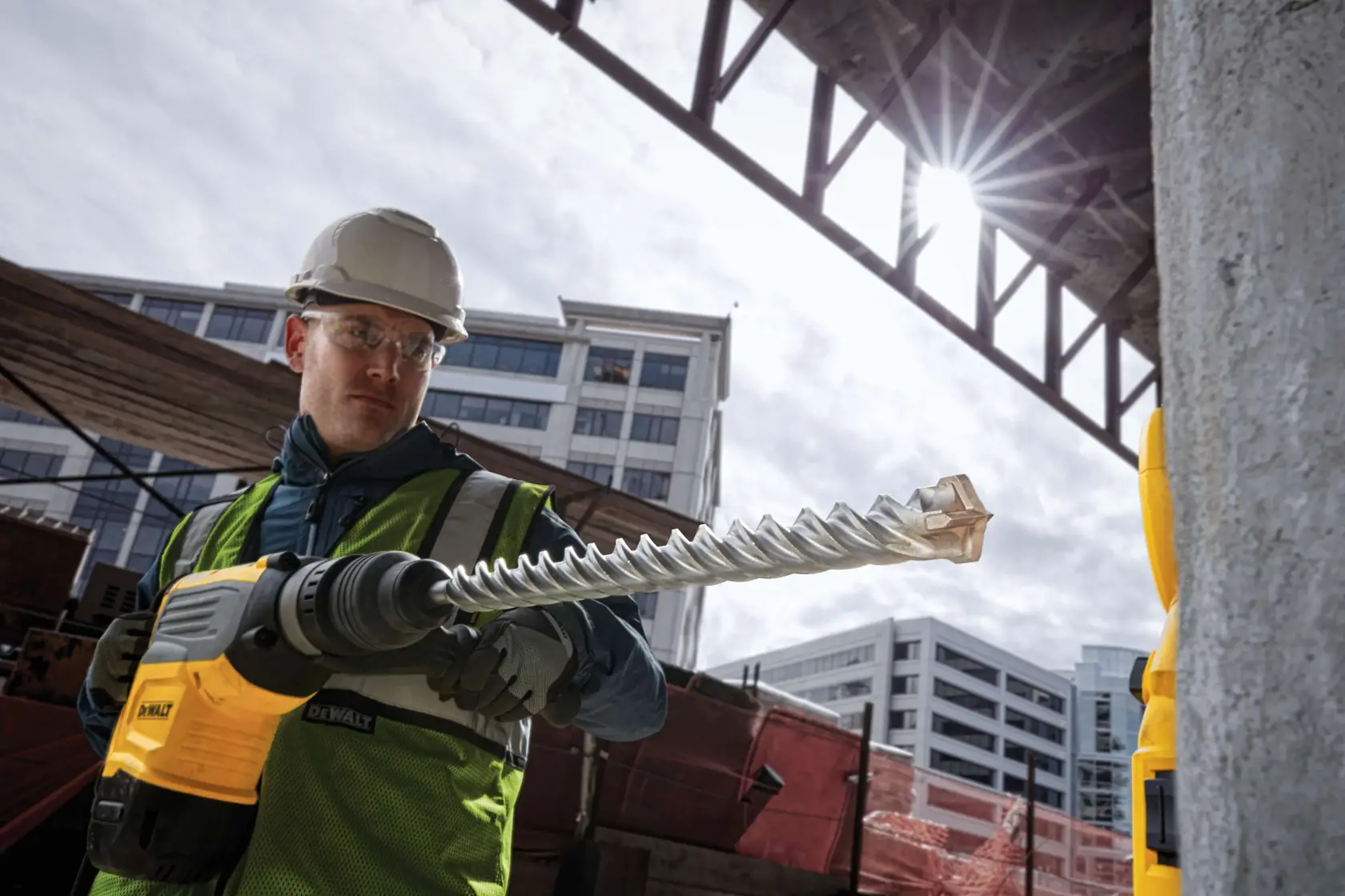 Trabajador DEWALT con taladro en obra, edificios urbanos al fondo.