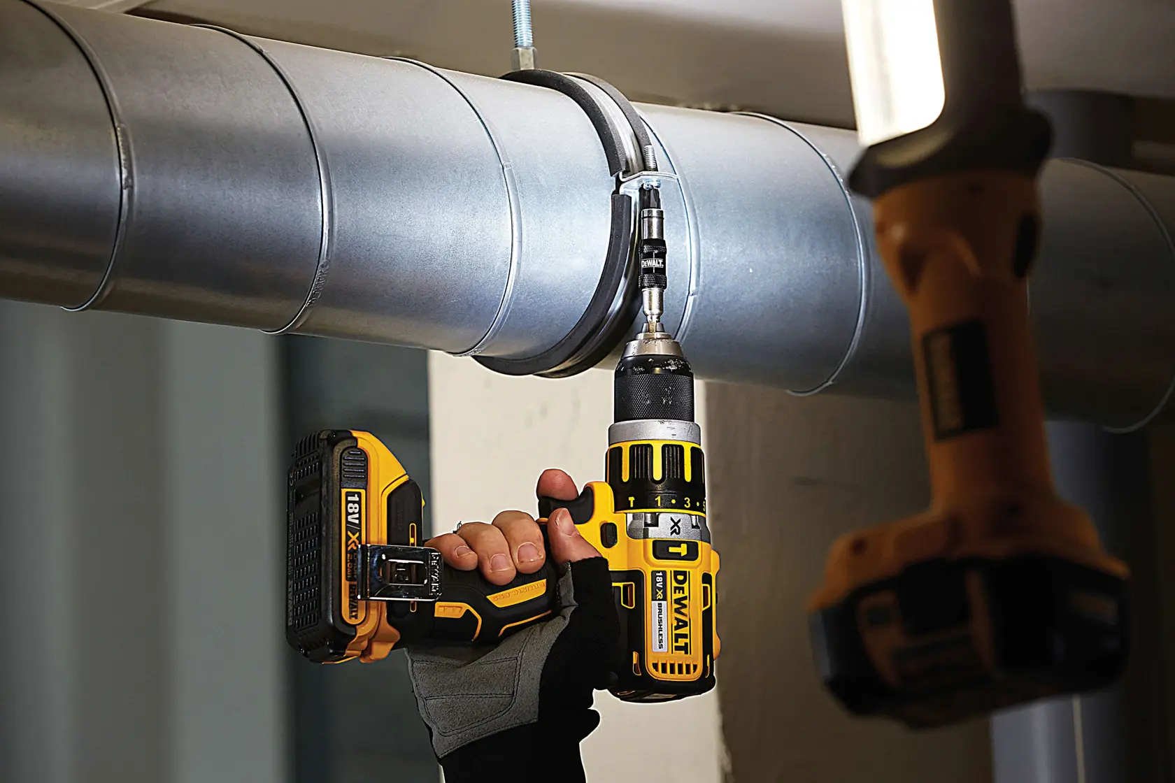 Hand uses a DEWALT cordless drill to fasten a screw into a metal pipe clamp in an industrial setting.