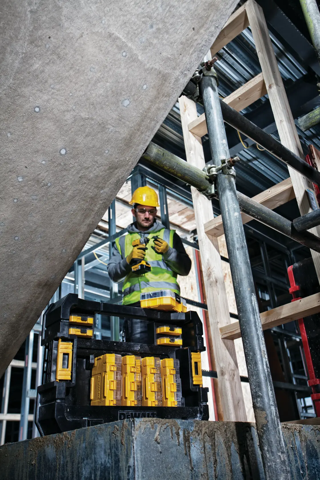 Kit DEWALT DT70716 en obra con trabajador, equipo de seguridad, andamios y estructura de madera al fondo.