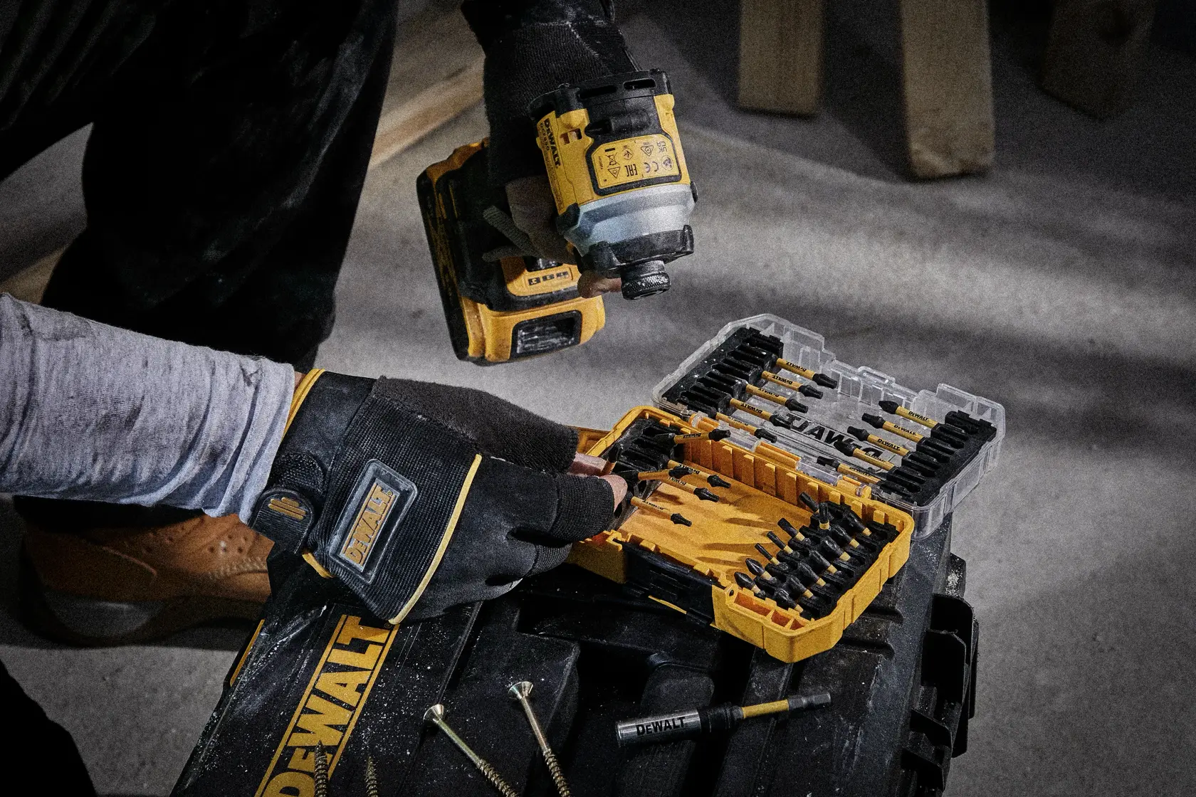 Person mit Handschuhen nutzt einen DEWALT-Bohrer und öffnet ein DEWALT-Bohrer-Set auf einem Werkzeugkasten.