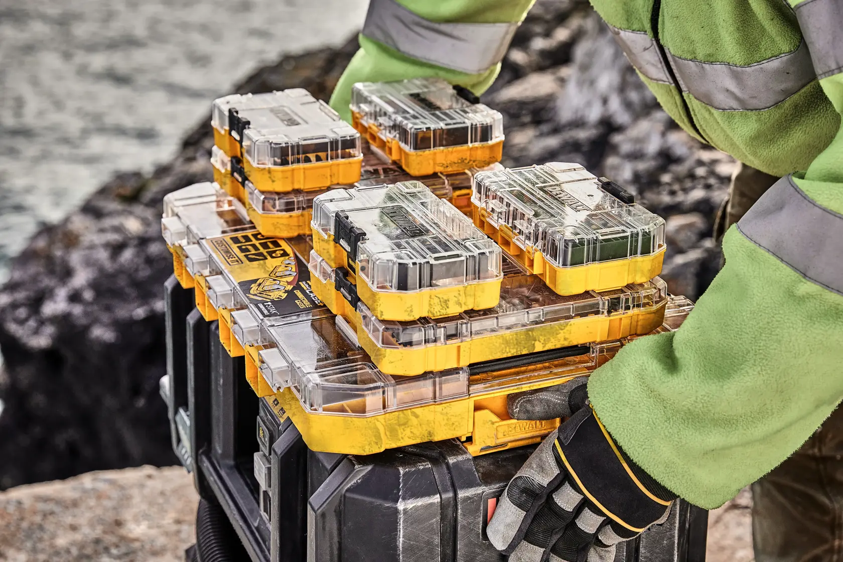 DEWALT DT70762 organizer boxes stacked outdoors, gloved hand adjusting them on a tool storage case.