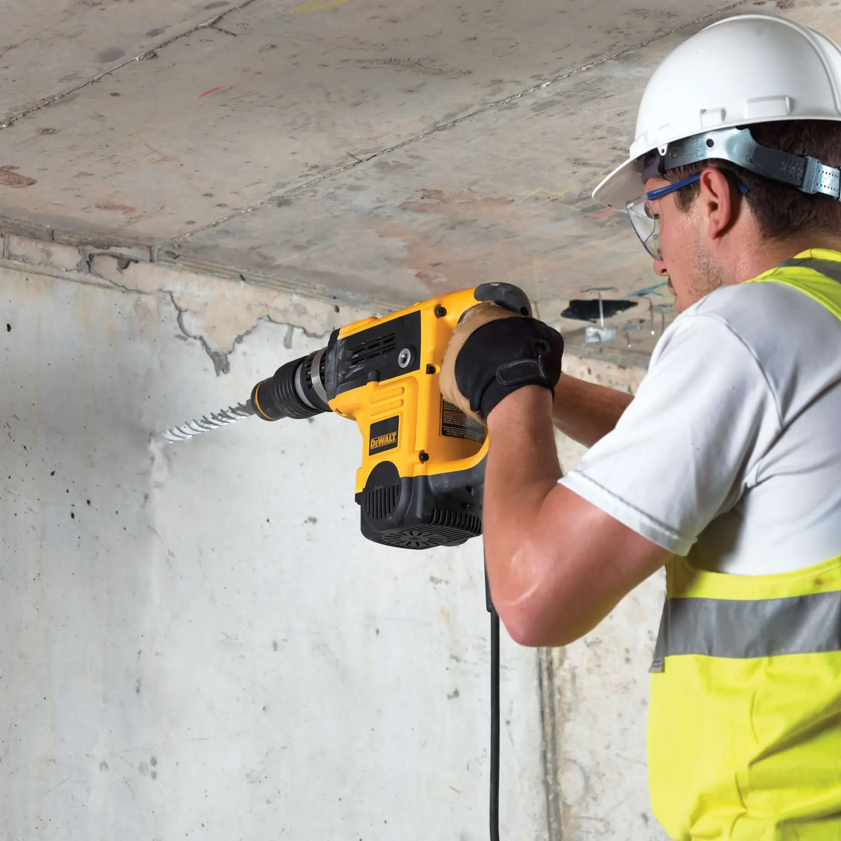 Person bohrt mit DEWALT DT9438 in eine Betonwand und trägt Sicherheitsausrüstung und Handschuhe.