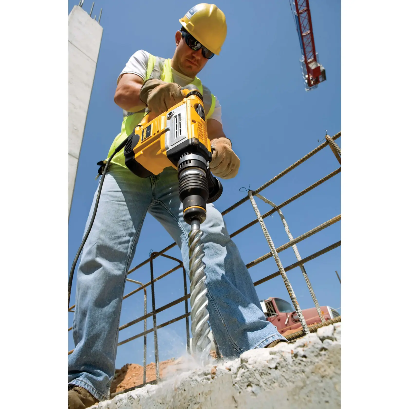 Arbeiter nutzt DEWALT Hammerbohrer auf Beton an einer Baustelle, mit Schutzkleidung und Handschuhen.