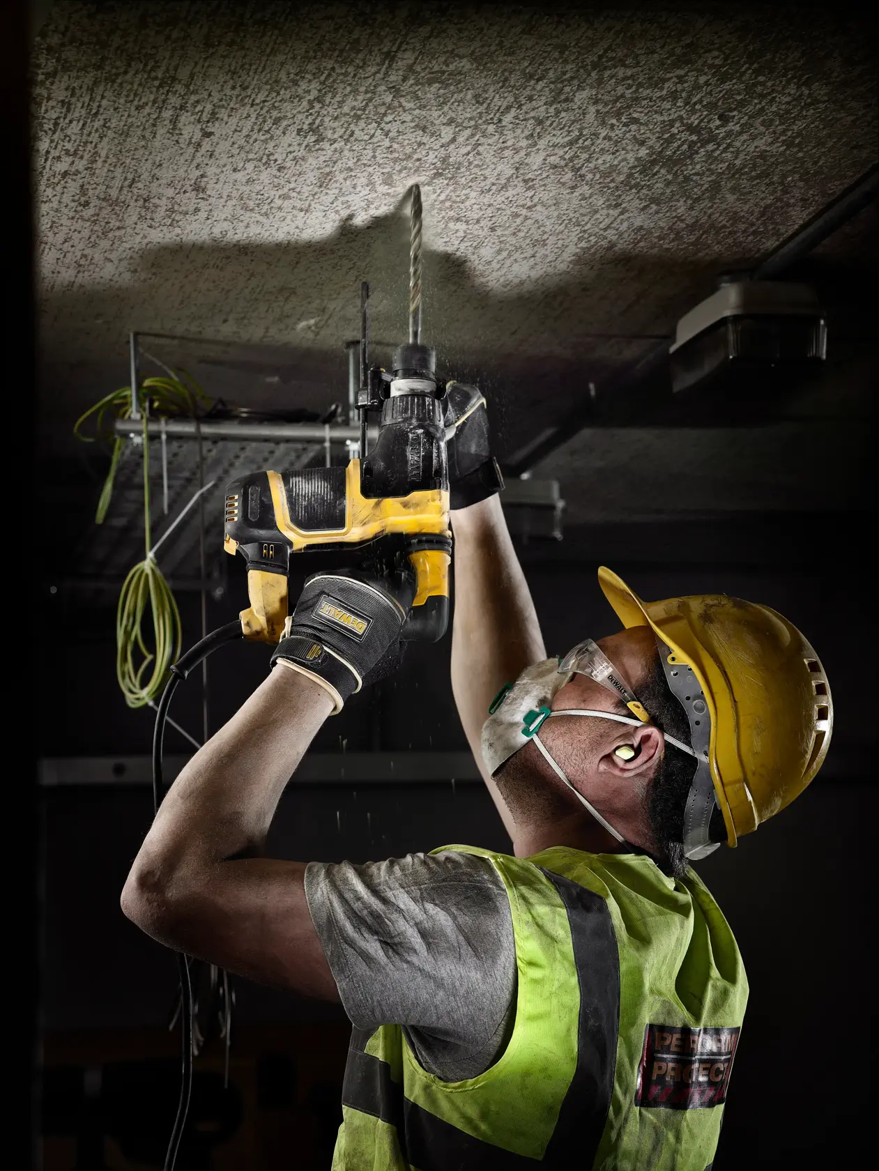 Trabajador con equipo de seguridad usa taladro DEWALT y broca DT9503 en techo de concreto.