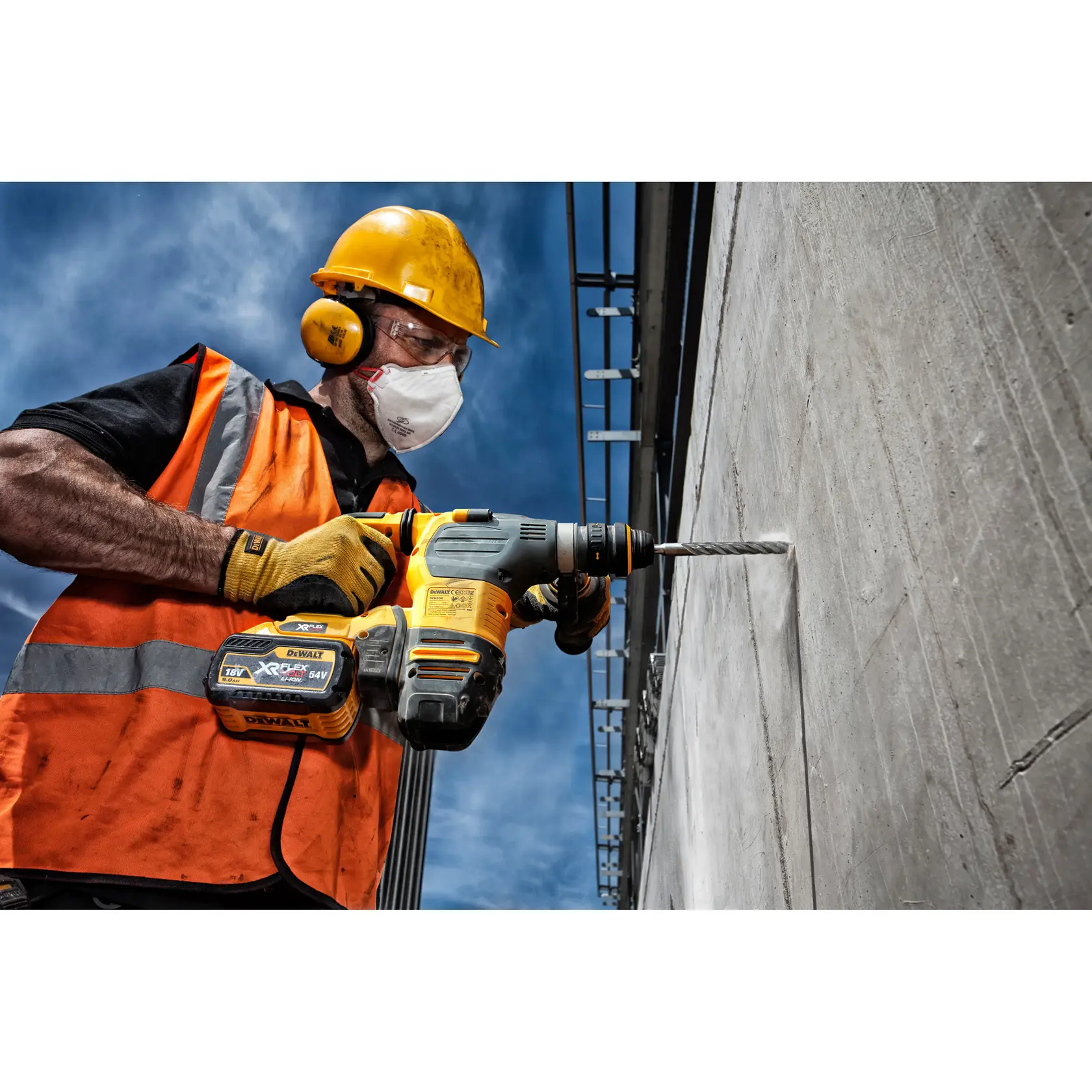 Trabajador usa taladro inalámbrico DEWALT DT9507 en muro de concreto, con protección, al aire libre.