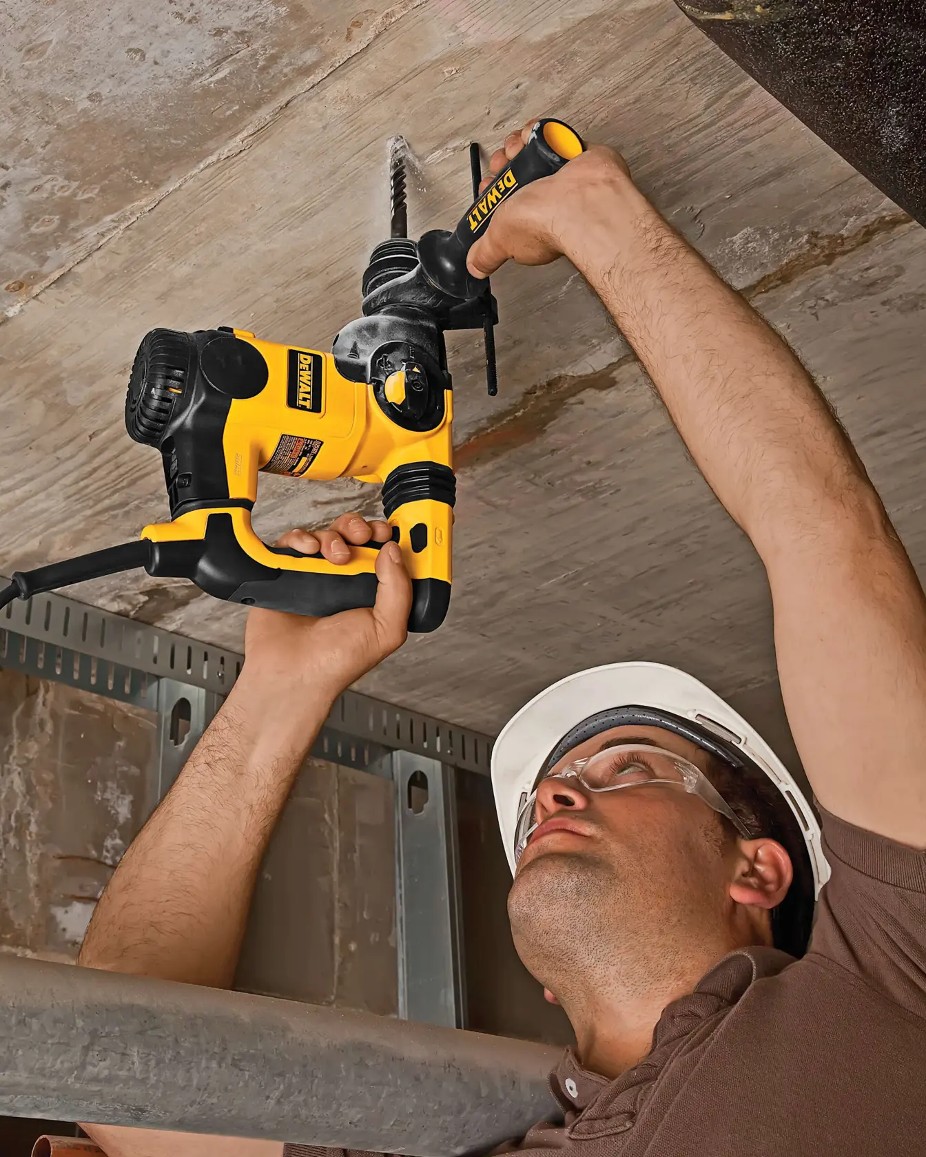 Persona usa taladro DEWALT en techo de concreto con casco de seguridad puesto.