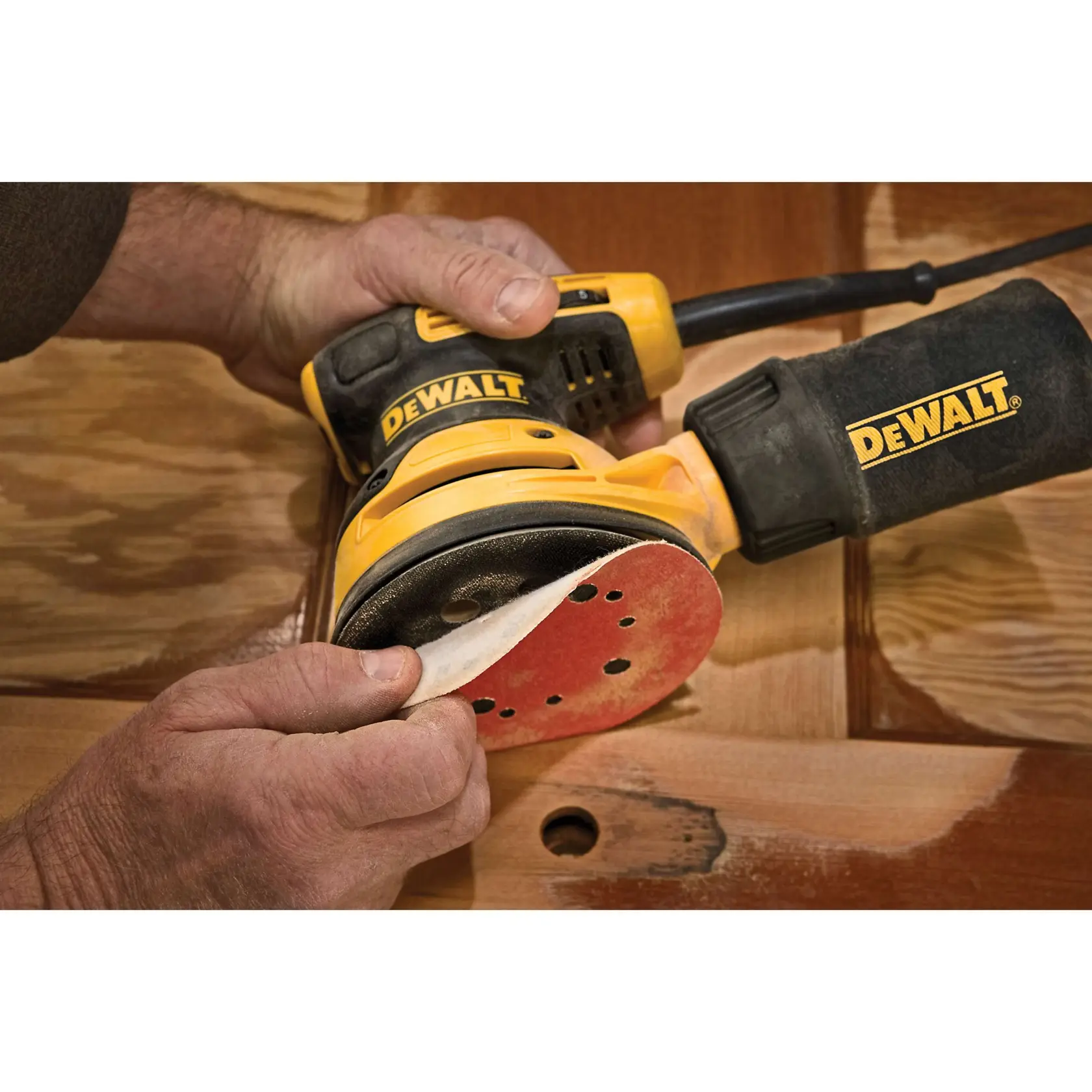 Elektrischer DEWALT-Orbitalschleifer mit Staubbeutel, gelb-schwarzes Design. Der darunter stehende Text lautet: 'Stabile Kontrolle mit gummierter Griffummantelung.'