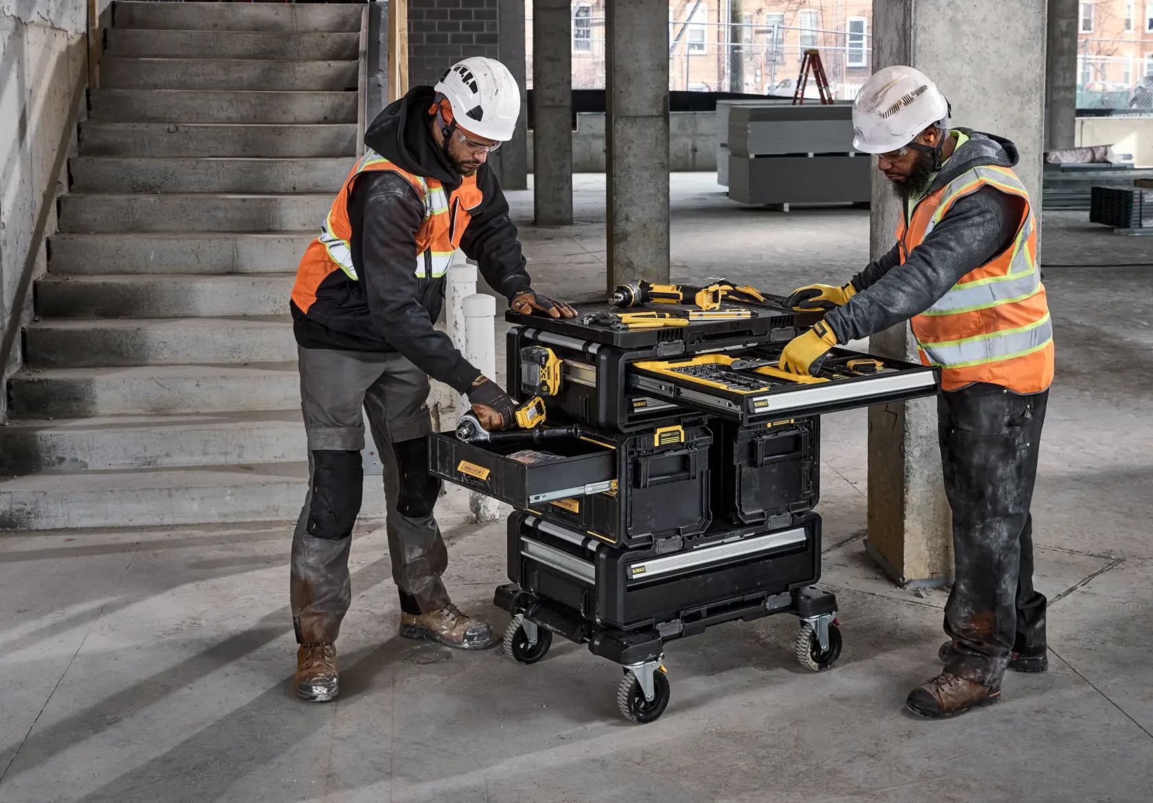 Zwei Arbeiter nutzen eine DEWALT Werkzeugstation mit offenen Schubladen auf einer Baustelle.
