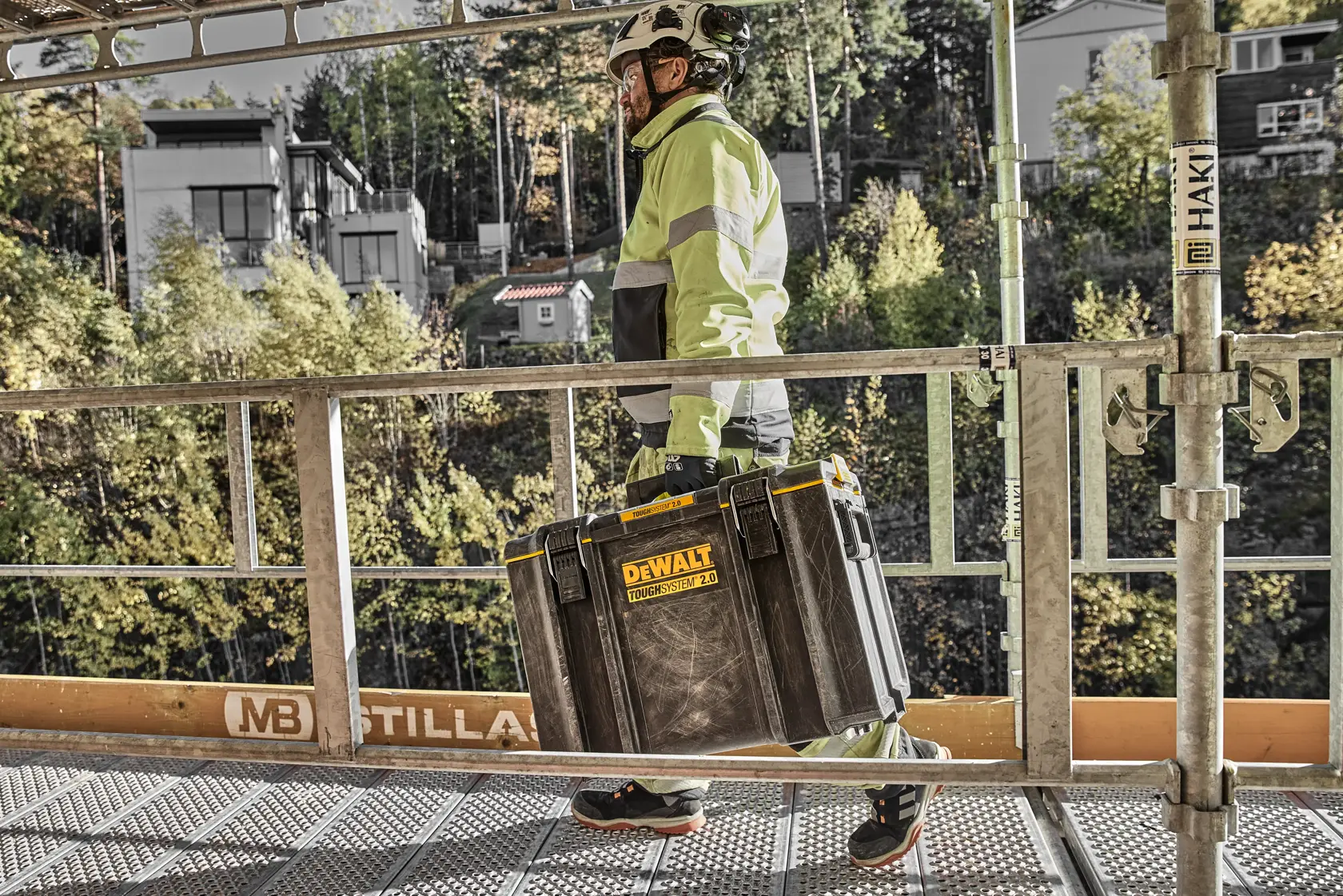 Person mit Sicherheitskleidung trägt DEWALT Toughsystem 2.0 Werkzeugkiste auf einer Baustelle.